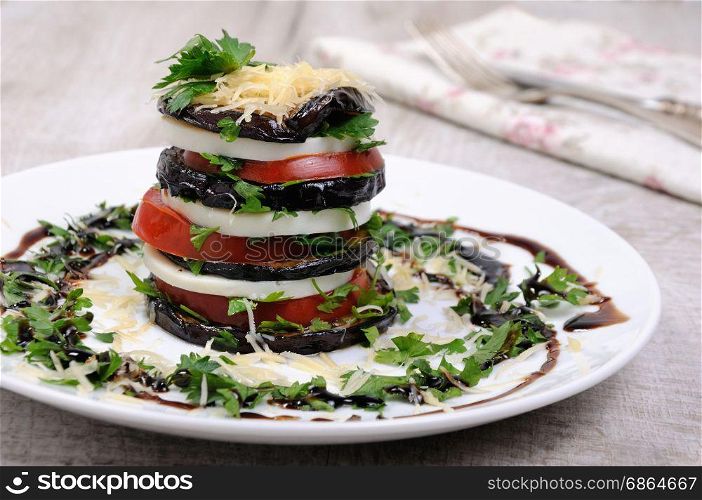 Appetizer from eggplant , slices of mozzarella combined in a pile with tomatoes spilled with herbs, seasoned Parmesan cheese