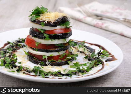 Appetizer from eggplant , slices of mozzarella combined in a pile with tomatoes spilled with herbs, seasoned Parmesan cheese