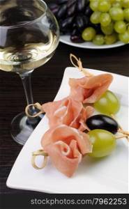 Appetizer of ham and grapes on a skewer with a glass of white wine