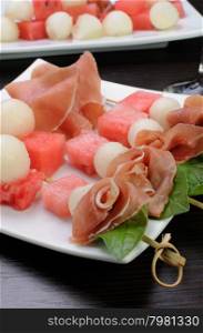 Appetizer of ham with melon and watermelon and basil on a skewer