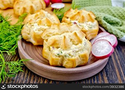 Appetizer of radish, dill, eggs and cheese in profiteroles on a clay plate, green cloth on a wooden boards background