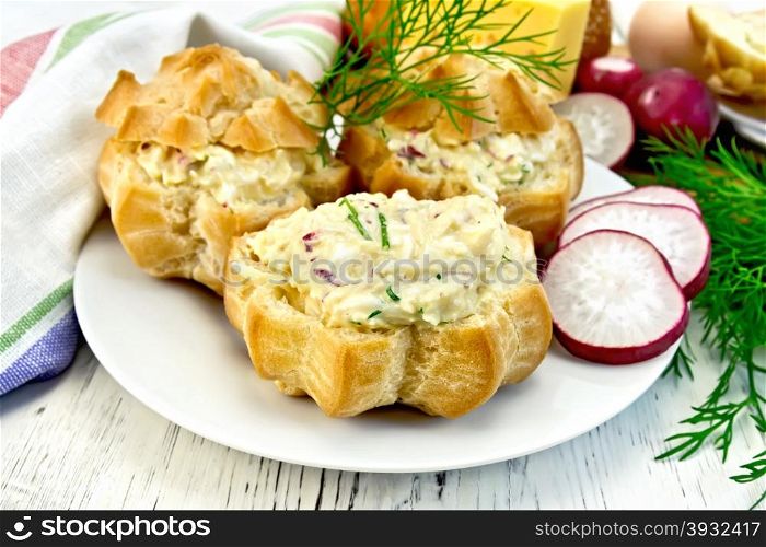 Appetizer of radish, dill, eggs and cheese in profiteroles on a white plate, napkin on the background light wooden boards