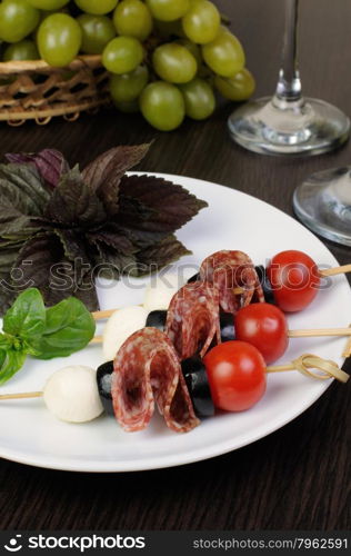 Appetizer of salami with mozzarella, olives, cherry tomatoes on skewers with basil