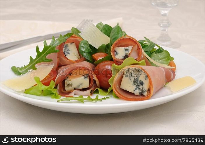 Appetizer rolls with jamon, blue cheese in the mix of lettuce and parmesan slices under