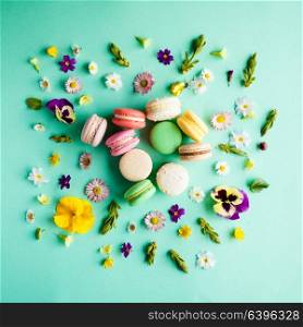 Appetizing colorful macaroons and beautiful flowers on green background. Flat layout. Colorful macaroons and flowers