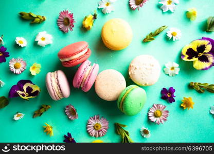 Appetizing colorful macaroons and beautiful flowers on green background. Flat layout. Colorful macaroons and flowers