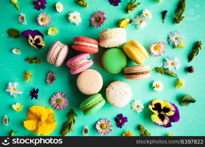 Appetizing colorful macaroons and beautiful flowers on green background. Flat layout. Colorful macaroons and flowers