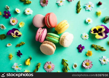 Appetizing colorful macaroons and beautiful flowers on green background. Flat layout. Colorful macaroons and flowers