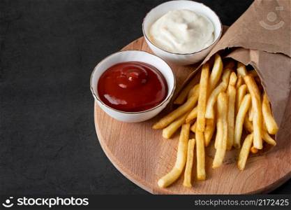 Appetizing crispy fries in an eco-friendly paper bag on a black background. Hot american fast food.. Appetizing crispy fries in an eco-friendly paper bag on black background. Hot american fast food.