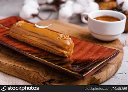 Appetizing eclair with caramel glaze and peanuts and coffee
