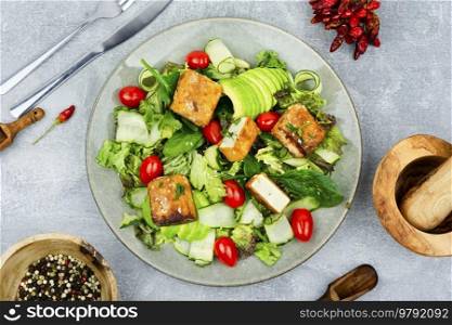 Appetizing lettuce salad, cucumber, avocado and breaded fried tofu soy cheese. Healthy lifestyle. Salad of roasted tofu and fresh vegetables, top view