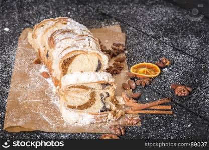 Appetizing looking sponge cake, homemade, sliced and displayed on the baking paper, filled with poppy seeds and walnuts, covered with powder sugar.