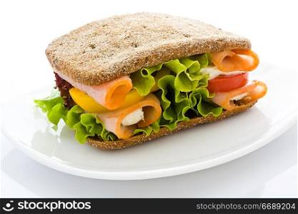 Appetizing sandwich from rye bread with a ham and salad on a white plate close up