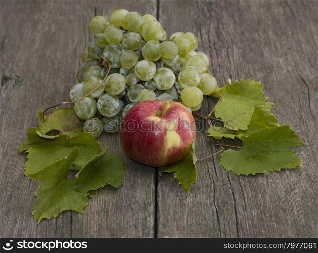 apple and cluster of grapes with leaves on a wooden table, a still life on a subject fruit of fall