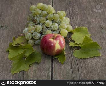 apple and cluster of grapes with leaves on a wooden table, a still life on a subject fruit of fall