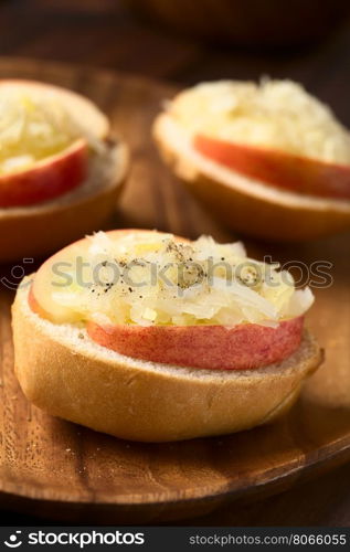 Apple and sauerkraut sandwich seasoned with black pepper on wooden plate, photographed with natural light (Selective Focus, Focus on the front of the apple slice and sauerkraut on the first sandwich)