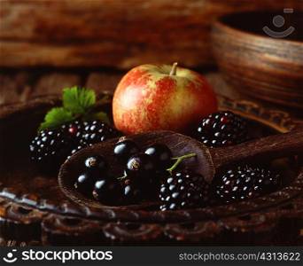 Apple, blackberries and blackcurrants in vintage wooden bowl with wooden spoon, close-up