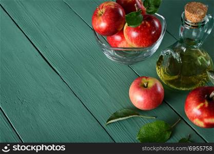 Apple cider vinegar and ripe red apples on background of green wooden table. Top view. Free space for text.