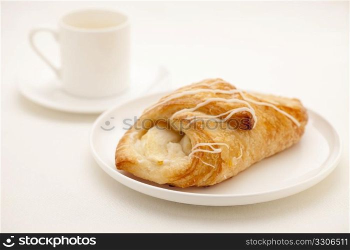 apple croissant pastry on white plate with a cup of espresso coffee in background