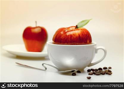 apple in a cup, saucer, spoon and coffee beans