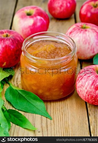 Apple jam in a glass jar, fresh red apples and leaves on wooden board