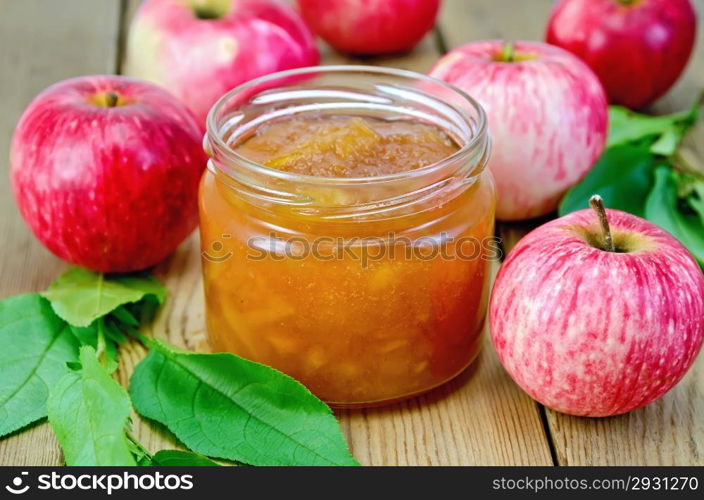 Apple jam in a glass jar, fresh red apples, twigs with leaves on a wooden board