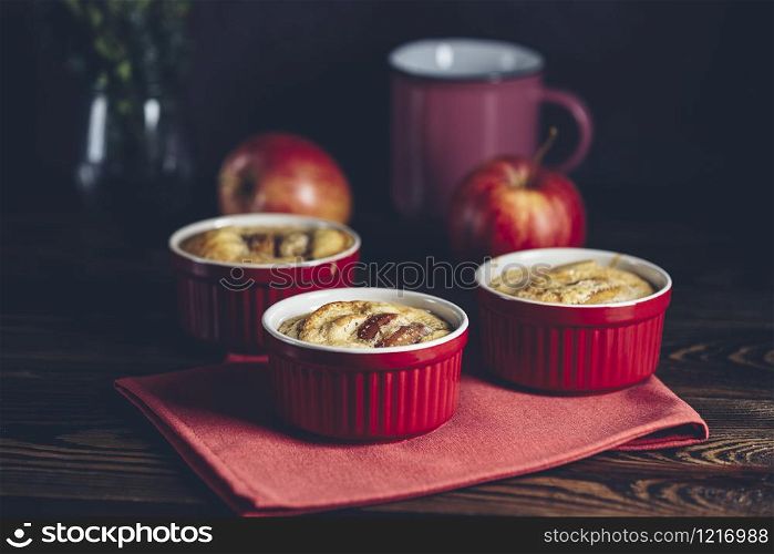 Apple pie in ceramic baking molds ramekin on dark wooden table. Close up, shallow depth of the field. Romantic breakfast or supper with coffee.