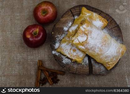 Apple strudel on wooden end of a tree with apples, cinnamon and star anise