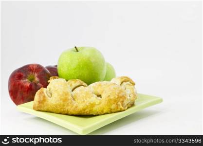 Apple strudel sits on light green, square plate with red and green apples behind