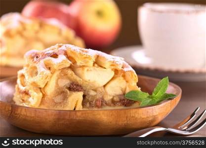 Apple strudel with raisins with coffee cup in back (Selective Focus, Focus on the left side of the apple-raisin stuffing and the front of the mint leaf)