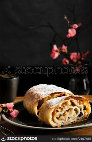 Apple strudel with walnuts and raisins, in the background a flowering branch of a spring shrub, close-up, selective focus. Baking for the day off.