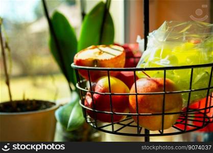 Apples and green grapes in a fruit basket in the kitchen, sunny day