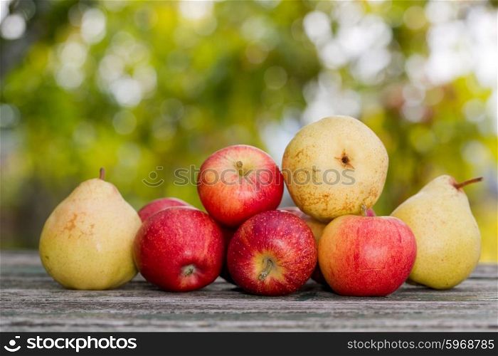 Apples and pears on wooden table over autumn bokeh background
