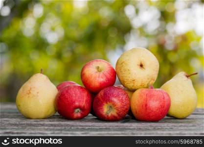 Apples and pears on wooden table over autumn bokeh background