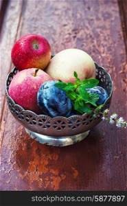 apples and plums in iron vase. apples and plums in iron vase on strensham wooden background