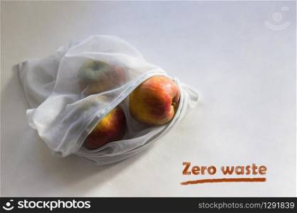 Apples in reusable fruit pouch in the sunlight with shadows. Chalk inscription Zero waste.