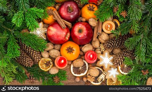 Apples, tangerine fruits, walnuts, cookies and spices with christmas tree branches. Festive food background