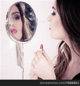Applying make up concept. Beautiful woman with red lipstick in front of mirror. Indoor.