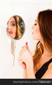 Applying make up concept. Beautiful woman with red lipstick in front of mirror. Indoor.