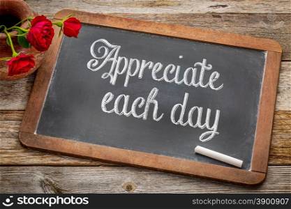 Appreciate each day - white chalk text on a vintage slate blackboard with red roses against rustic wood