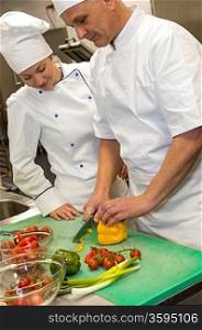Apprentice learning cutting vegetables from chef in kitchen