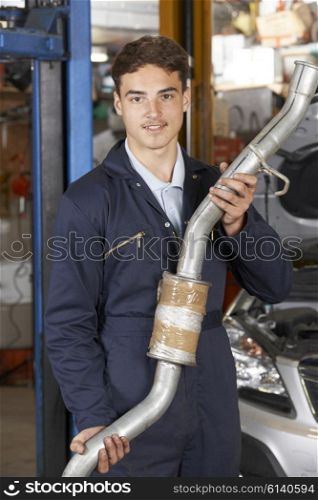 Apprentice Mechanic Holding Exhaust Pipe In Auto Repair Shop