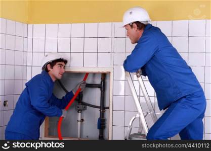 Apprentice passing red cable up behind a tiled wall