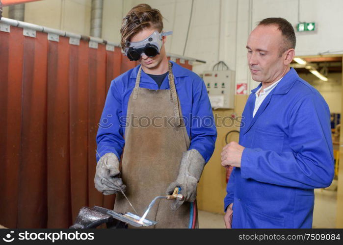 Apprentice using blowtorch, supervisor watching