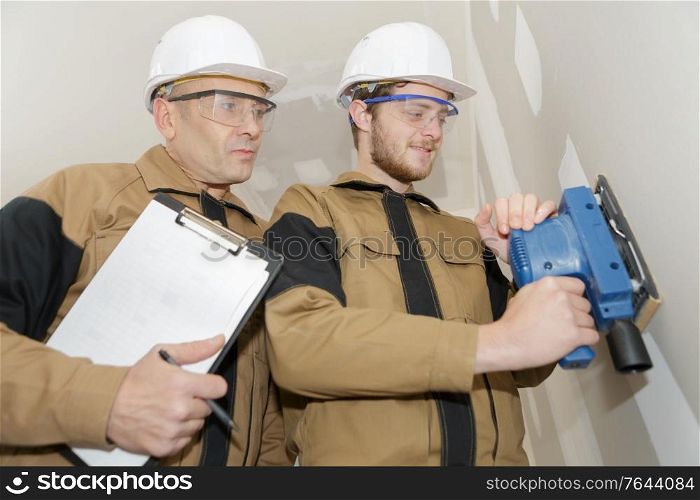 apprentice using sander on wall under supervision