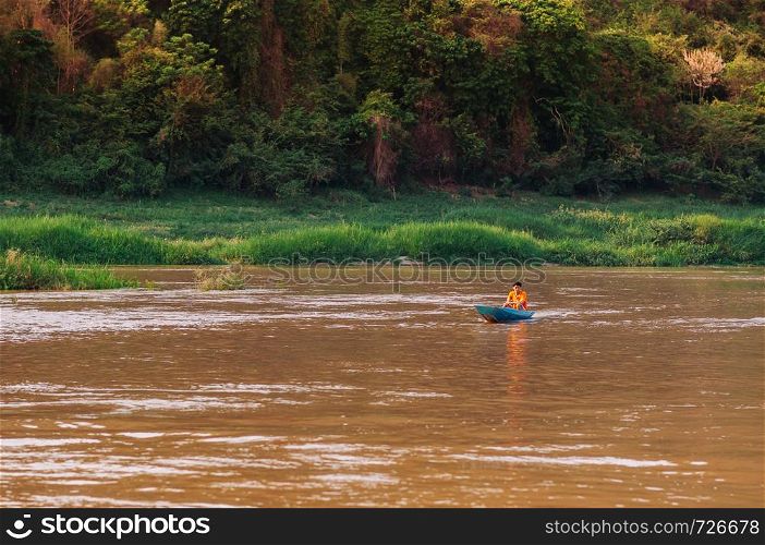 APR 3,2018 Luang Prabang, Laos - Asian local fisherman on blue wooden boat and rural scene of Mae khong river with lush green shoreline