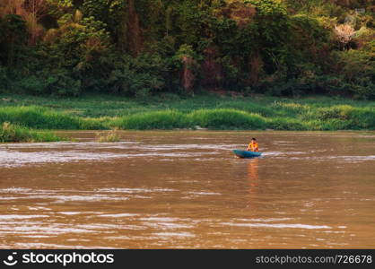 APR 3,2018 Luang Prabang, Laos - Asian local fisherman on blue wooden boat and rural scene of Mae khong river with lush green shoreline