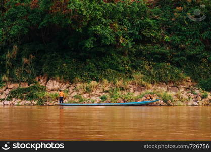 APR 3,2018 Luang Prabang, Laos - Asian local fisherman on blue wooden boat and rural scene of Mae khong river with lush green shoreline