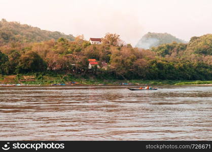 APR 3,2018 Luang Prabang, Laos - Small Row boat with monks in Mekong river with mountain top temple during summer with soft evening light