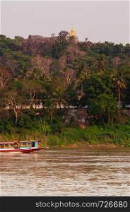 APR 3,2018 Luang Prabang, Laos - Vintage colourful wooden boats in yellow Mekong river during summer with soft evening light and Mount Phousi pagoda